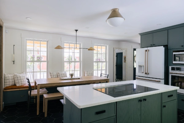 Open-concept kitchen with white waterfall island, induction cooktop, green cabinetry, and adjacent dining nook with bench seating